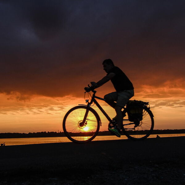 Ein Fahrradfahrer fährt in der Abenddämmerung am Flussufer.
