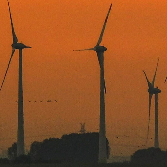 Mehrere Windräder in der Abenddämmerung am Meer.