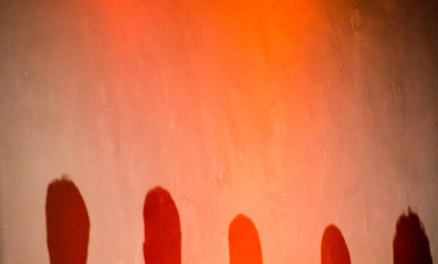Schatten von Menschen an einer rot beleuchteten Wand.