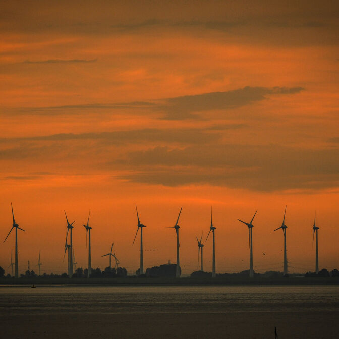 Mehrere Windräder in der Abenddämmerung am Meer.